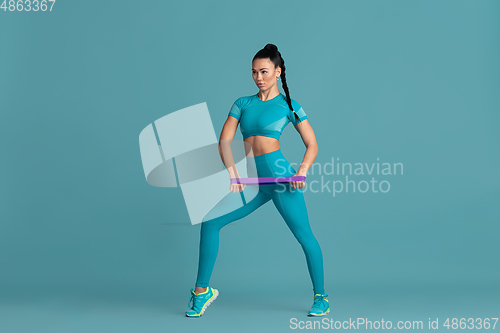 Image of Beautiful young female athlete practicing on blue studio background, monochrome portrait