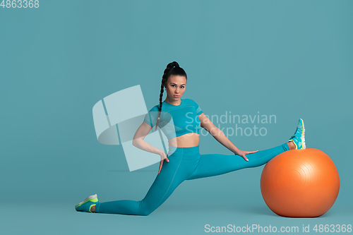 Image of Beautiful young female athlete practicing on blue studio background, monochrome portrait