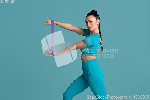 Image of Beautiful young female athlete practicing on blue studio background, monochrome portrait