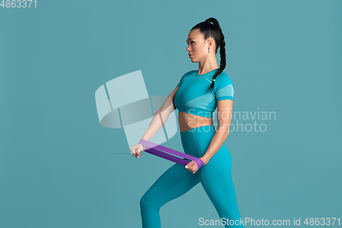 Image of Beautiful young female athlete practicing on blue studio background, monochrome portrait