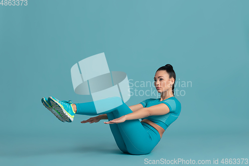 Image of Beautiful young female athlete practicing on blue studio background, monochrome portrait