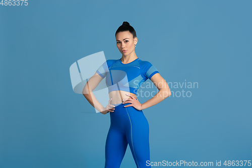 Image of Beautiful young female athlete practicing on blue studio background, monochrome portrait