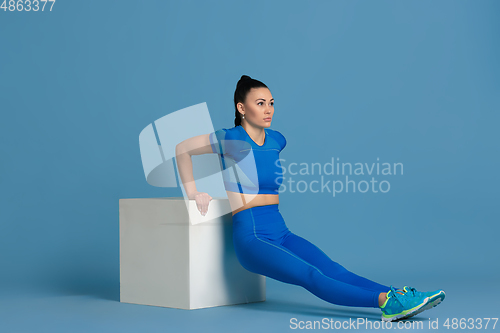 Image of Beautiful young female athlete practicing on blue studio background, monochrome portrait