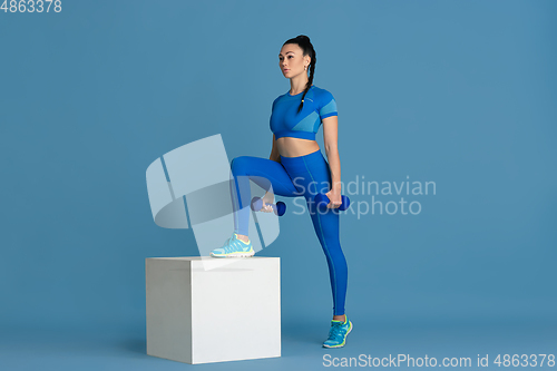 Image of Beautiful young female athlete practicing on blue studio background, monochrome portrait