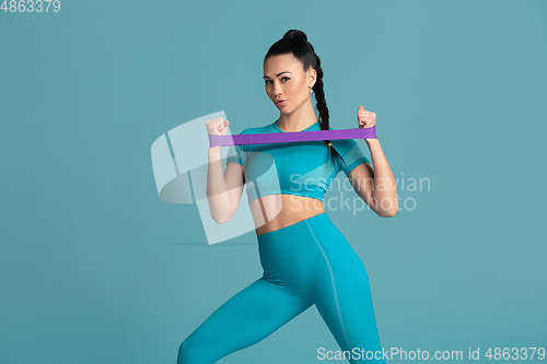 Image of Beautiful young female athlete practicing on blue studio background, monochrome portrait