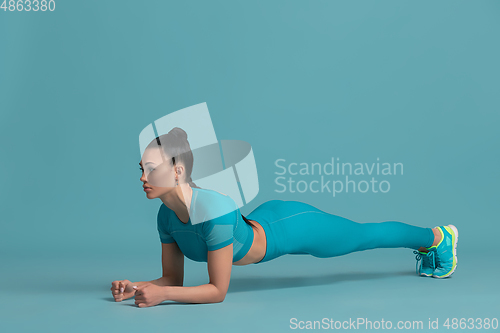 Image of Beautiful young female athlete practicing on blue studio background, monochrome portrait