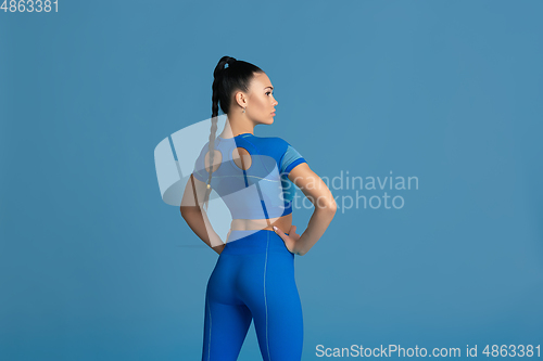 Image of Beautiful young female athlete practicing on blue studio background, monochrome portrait