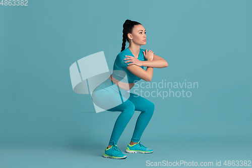 Image of Beautiful young female athlete practicing on blue studio background, monochrome portrait