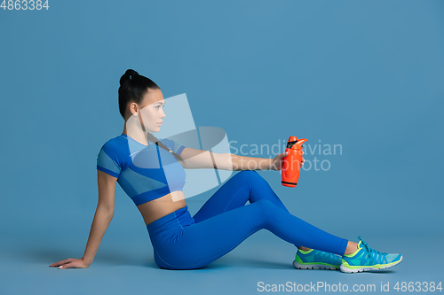 Image of Beautiful young female athlete practicing on blue studio background, monochrome portrait