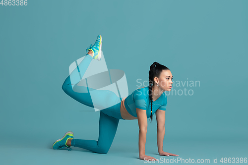 Image of Beautiful young female athlete practicing on blue studio background, monochrome portrait