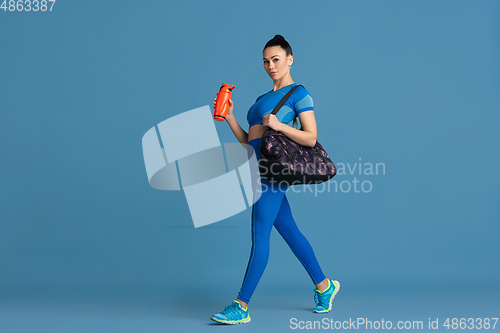 Image of Beautiful young female athlete practicing on blue studio background, monochrome portrait