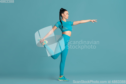 Image of Beautiful young female athlete practicing on blue studio background, monochrome portrait