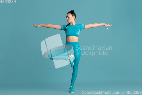 Image of Beautiful young female athlete practicing on blue studio background, monochrome portrait