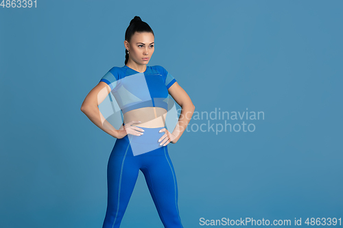 Image of Beautiful young female athlete practicing on blue studio background, monochrome portrait