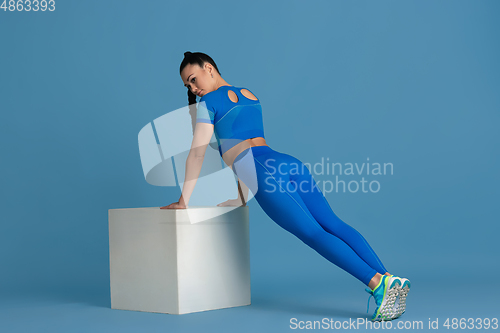 Image of Beautiful young female athlete practicing on blue studio background, monochrome portrait