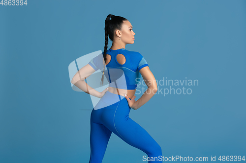 Image of Beautiful young female athlete practicing on blue studio background, monochrome portrait