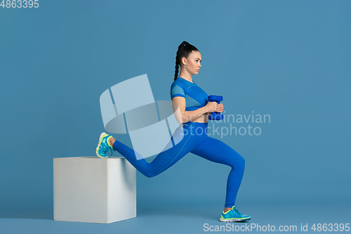 Image of Beautiful young female athlete practicing on blue studio background, monochrome portrait