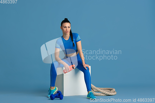 Image of Beautiful young female athlete practicing on blue studio background, monochrome portrait