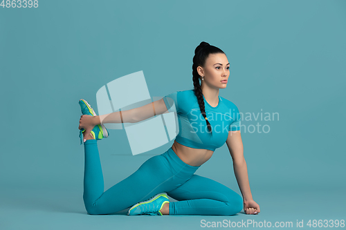 Image of Beautiful young female athlete practicing on blue studio background, monochrome portrait