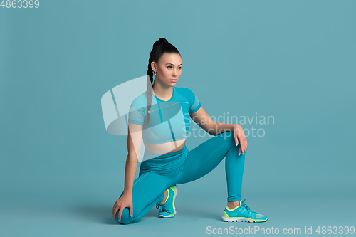 Image of Beautiful young female athlete practicing on blue studio background, monochrome portrait