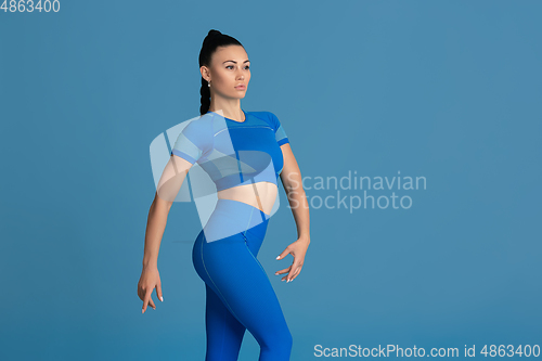 Image of Beautiful young female athlete practicing on blue studio background, monochrome portrait