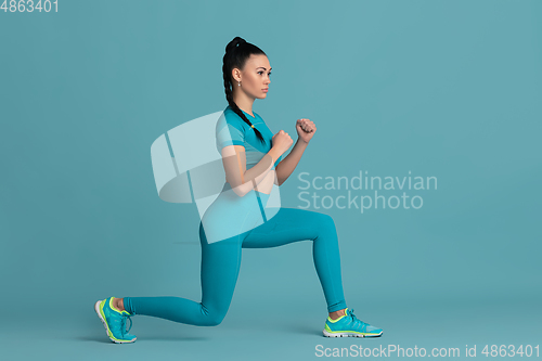 Image of Beautiful young female athlete practicing on blue studio background, monochrome portrait