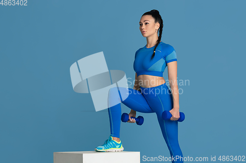 Image of Beautiful young female athlete practicing on blue studio background, monochrome portrait