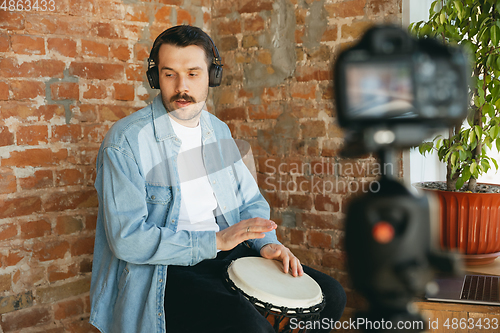 Image of Caucasian musician playing hand drum during online concert at home isolated and quarantined, inspired improvising