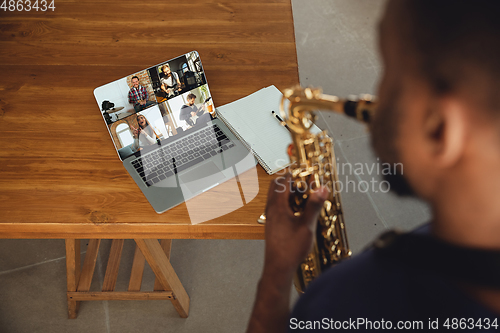 Image of African-american musician playing saxophone during online concert or sound-check connected with the band at home isolated and quarantined