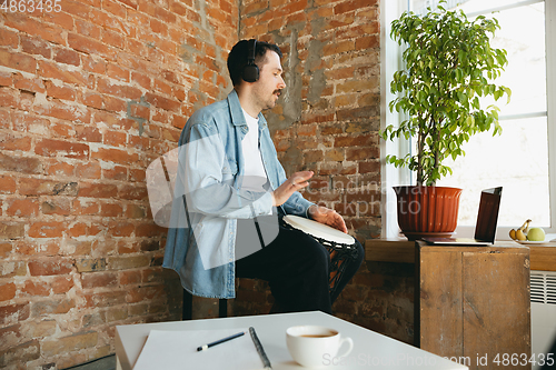 Image of Caucasian musician playing hand drum during online concert at home isolated and quarantined, improvising