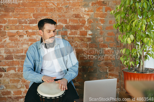 Image of Caucasian musician playing hand drum during online concert at home isolated and quarantined, inspired improvising