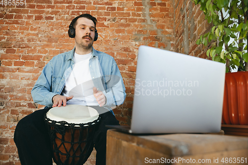 Image of Caucasian musician playing hand drum during online concert at home isolated and quarantined, improvising