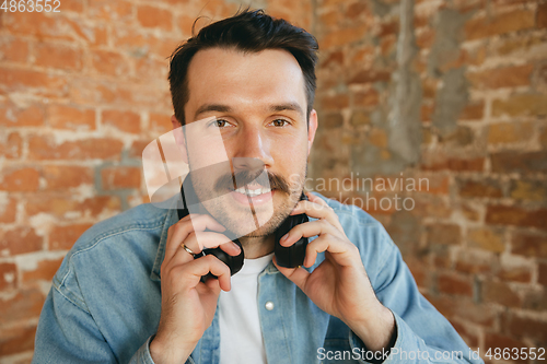 Image of Caucasian musician in headphones greeting audience before online concert at home isolated and quarantined, cheerful, smiling