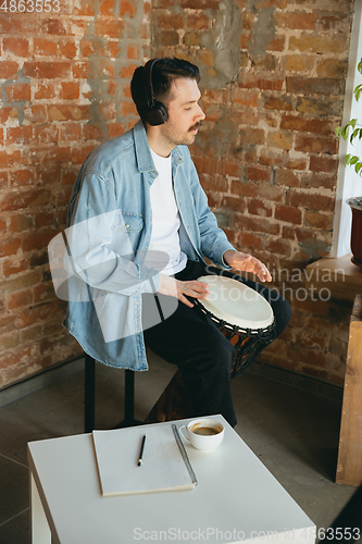 Image of Caucasian musician playing hand drum during online concert at home isolated and quarantined, inspired improvising