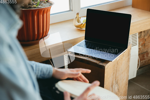 Image of Caucasian musician playing hand drum during online concert at home isolated and quarantined, close up, blank laptop screen, copyspace