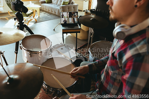 Image of Caucasian musician playing drumms during online concert or sound-check with the band at home isolated and quarantined, focus on laptop