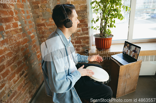 Image of Caucasian musician playing hand drum during concert at home isolated and quarantined, playing with the band in online streaming, conference