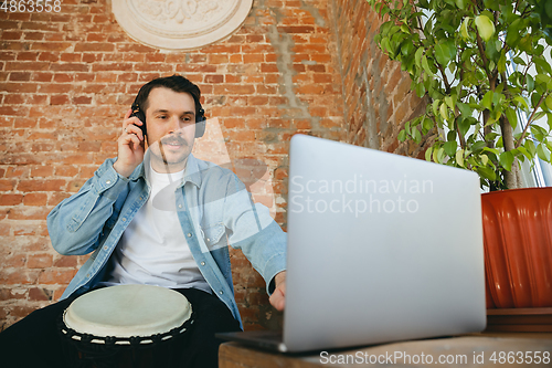 Image of Caucasian musician playing hand drum during online concert at home isolated and quarantined, inspired improvising