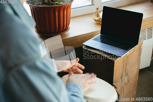 Image of Caucasian musician playing hand drum during online concert at home isolated and quarantined, focus on blank laptop screen, copyspace