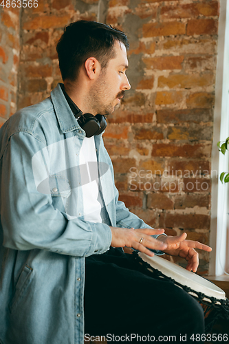 Image of Caucasian musician playing hand drum during online concert at home isolated and quarantined, inspired improvising