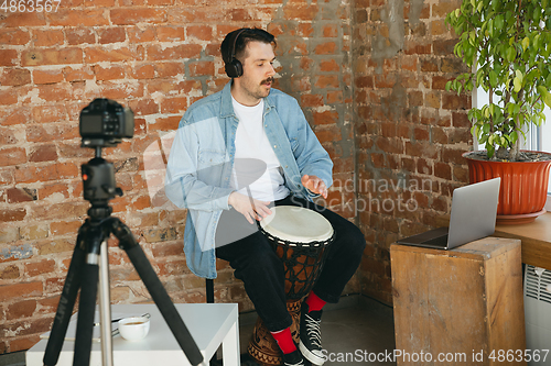 Image of Caucasian musician playing hand drum during online concert at home isolated and quarantined, inspired improvising