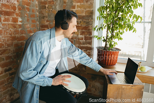 Image of Caucasian musician playing hand drum during online concert at home isolated and quarantined, inspired improvising