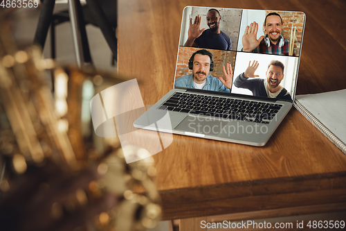 Image of African-american musician playing saxophone during online concert or sound-check connected with the band at home quarantined, focus on laptop