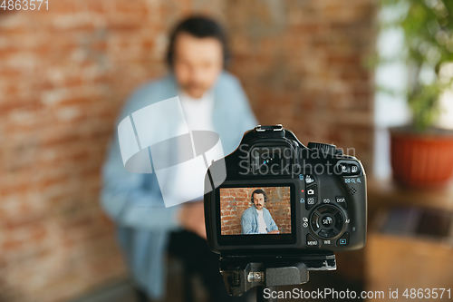 Image of Caucasian musician playing hand drum during online concert at home isolated and quarantined, focus on camera