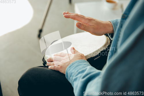 Image of Caucasian musician playing hand drum during online concert at home isolated and quarantined, close up