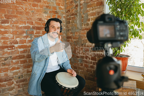 Image of Caucasian musician playing hand drum during online concert at home isolated and quarantined, smiling, thumb up