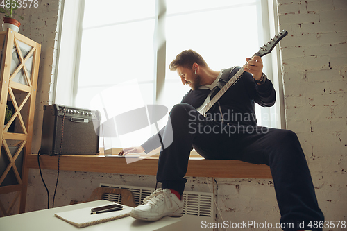 Image of Caucasian musician playing guitar during online concert at home isolated and quarantined, tuning the stream