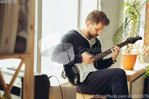 Image of Caucasian musician playing guitar during online concert at home isolated and quarantined, cheerful improvising