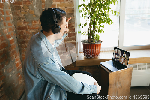 Image of Caucasian musician playing hand drum during concert at home isolated and quarantined, playing with the band in online streaming, conference