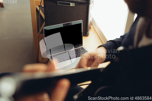 Image of Caucasian musician playing guitar during concert at home isolated and quarantined, cheerful improvising, focus on blank laptop screen